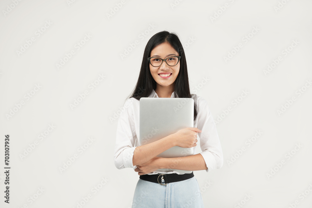 An Asian woman smiles confidently while hugging her laptop, showcasing warmth and professionalism in a bright, modern setting. An Asian woman smiles confidently while hugging her laptop, showcasing warmth and professionalism in a bright, modern setting.
