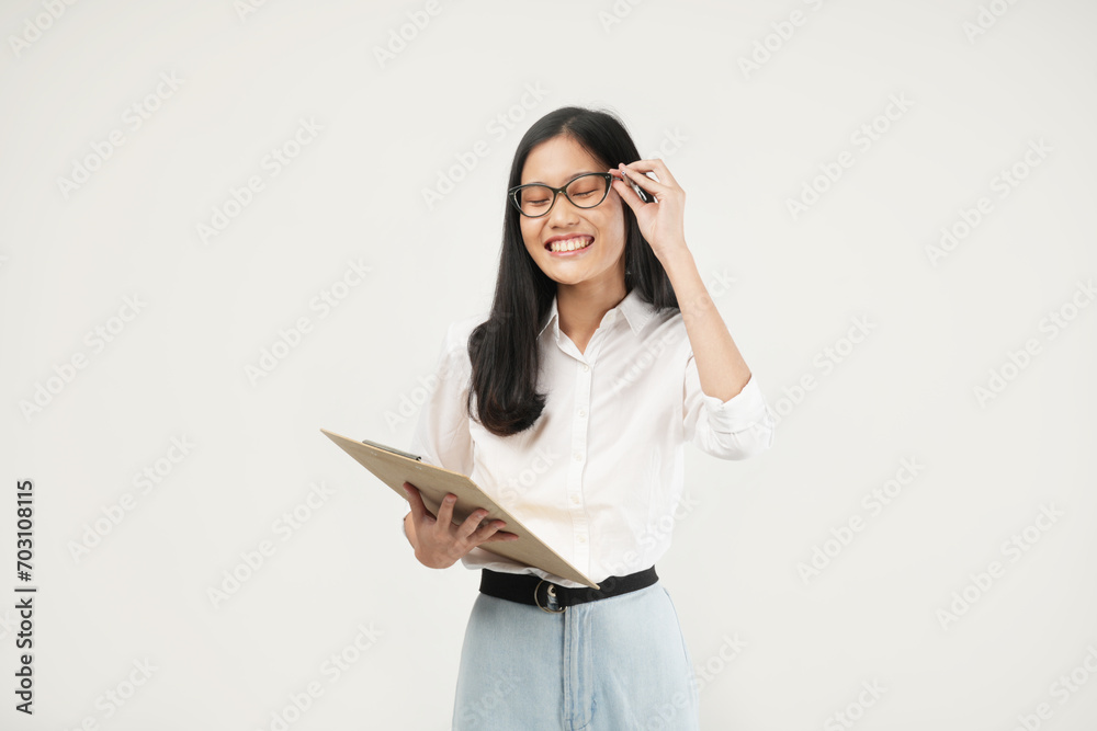 An Asian woman smiles warmly while writing on a clipboard, exuding confidence and positivity in a professional setting.