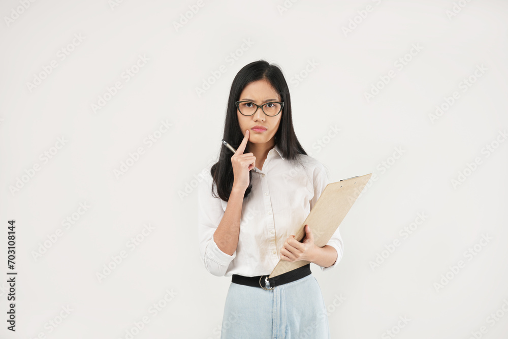 An Asian woman holds a clipboard and pen, thoughtfully tapping her chin with the pen while appearing deep in concentration in a professional setting An Asian woman holds a clipboard and pen, thoughtfully tapping her chin with the pen while appearing deep in concentration in a professional setting
