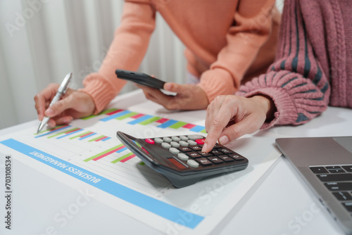 two individuals are engaged in accounting work. One person is wearing a pink sweater, and they both are reviewing financial charts and graphs, likely for a small business.