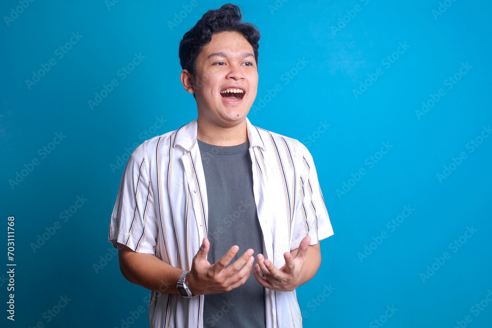 Excited young Asian man looking away while smiling over blue background Excited young Asian man looking away while smiling over blue background
