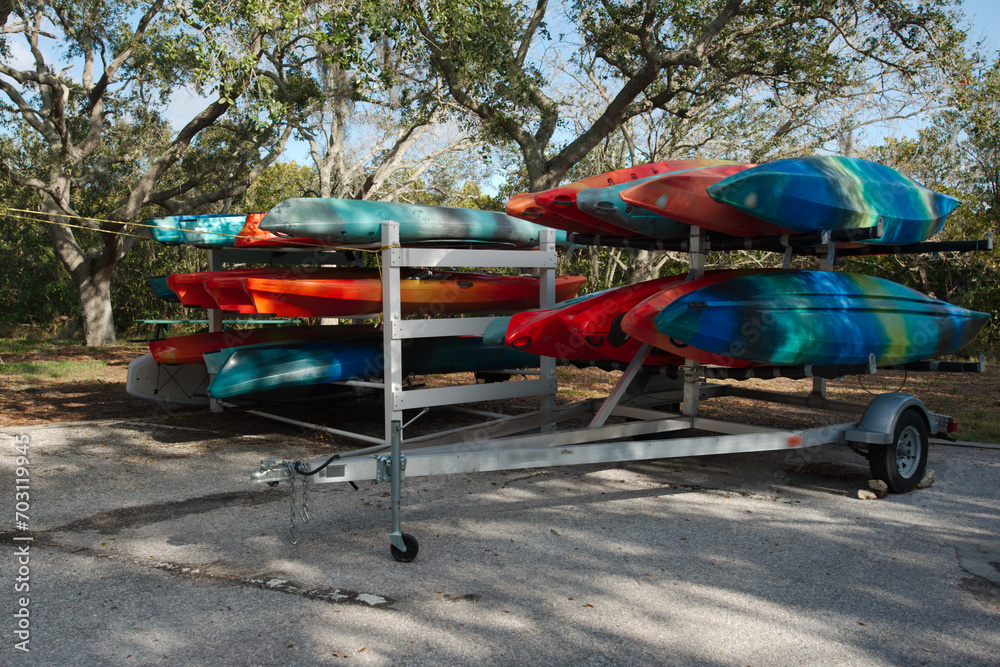 Multiple colored red, blue,orange and green Kyacks on a metal trailer.Green trees, grass and blue sky on a sunny day with a blue sky in Florida.