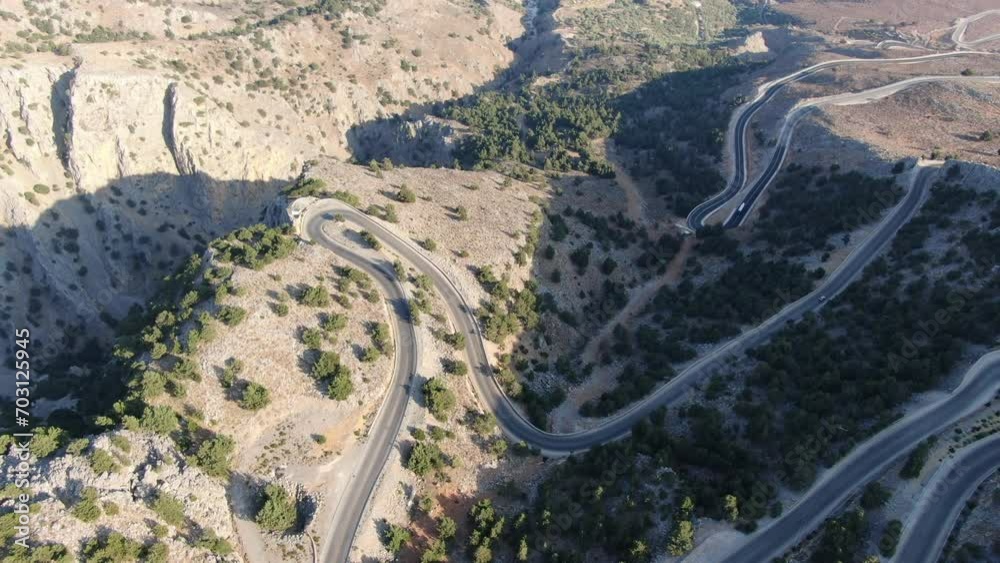 Drone view in Greece flying over a brown and green mountain with serpent road and sea on the horizon on a sunny day Drone view in Greece flying over a brown and green mountain with serpent road and sea on the horizon on a sunny day