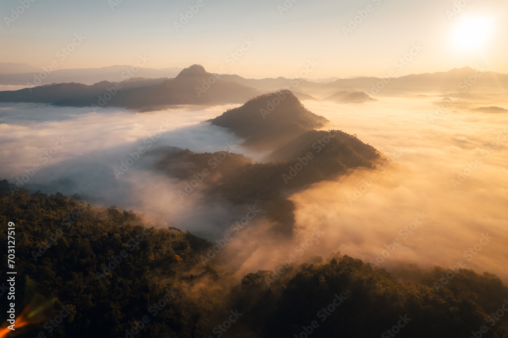 Aerial view of forest and mountain in fog with golden sunbeams at sunrise Aerial view of forest and mountain in fog with golden sunbeams at sunrise
