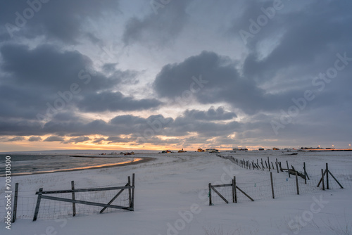 Snowy beach at sunset with a fence and a village in the background on a cold winter day, Skallelv, Northern Norway photo