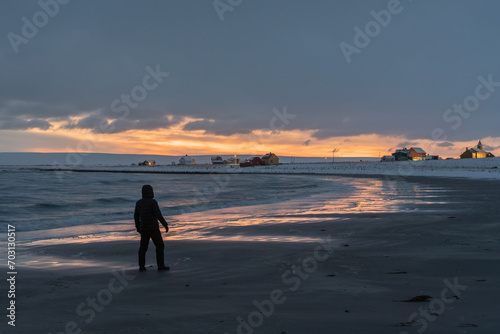 Moody afternoon sky and reflections on wet sand by the sea on a winter afternoon. Man standing and watching the view. Skallelv, Northern Norway photo