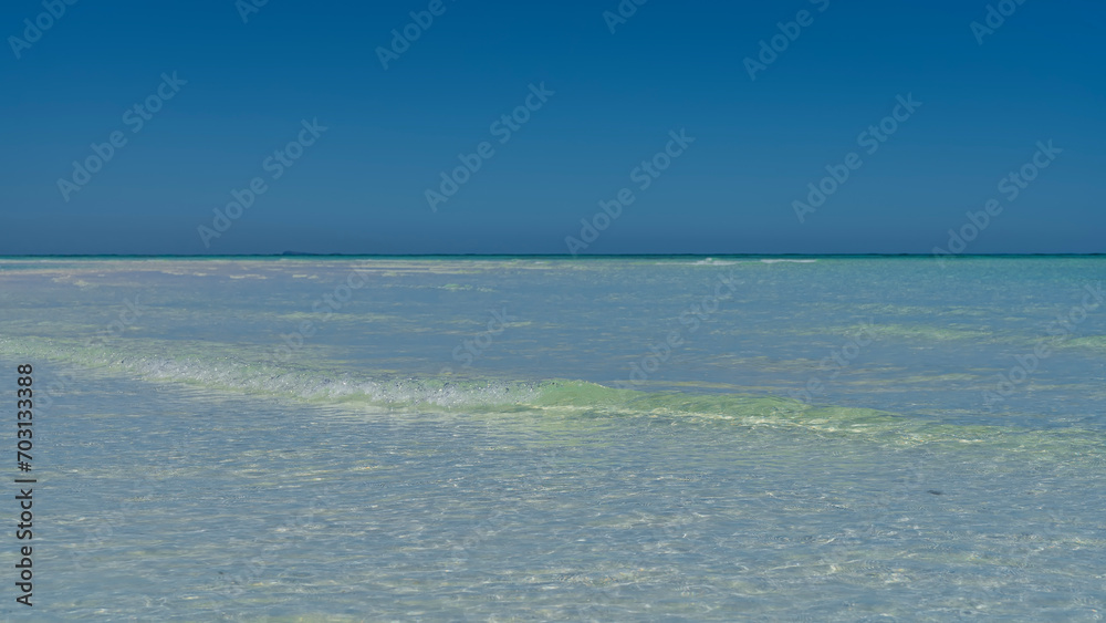 Obraz premium A beautiful aquamarine ocean with crystal clear water. The waves are foaming towards the shore. Blue sky. Copy space. Minimalism. Madagascar. Nosy Iranja 