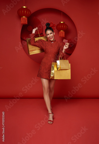 Happy Asian shopaholic woman wearing traditional cheongsam qipao dress holding shopping bag and credit card isolated on red background. Happy Chinese new year © NaMong Productions