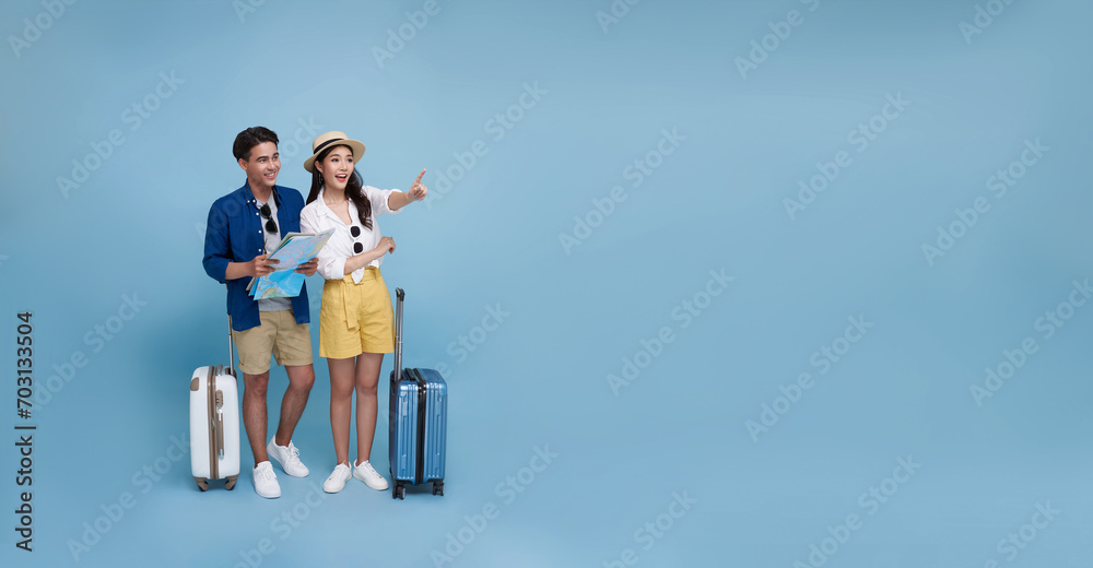 Happy Asian couple tourist looking map and hand pointing to copy space with baggage going to travel on holidays isolated on blue panorama background. Happy Asian couple tourist looking map and hand pointing to copy space with baggage going to travel on holidays isolated on blue panorama background.