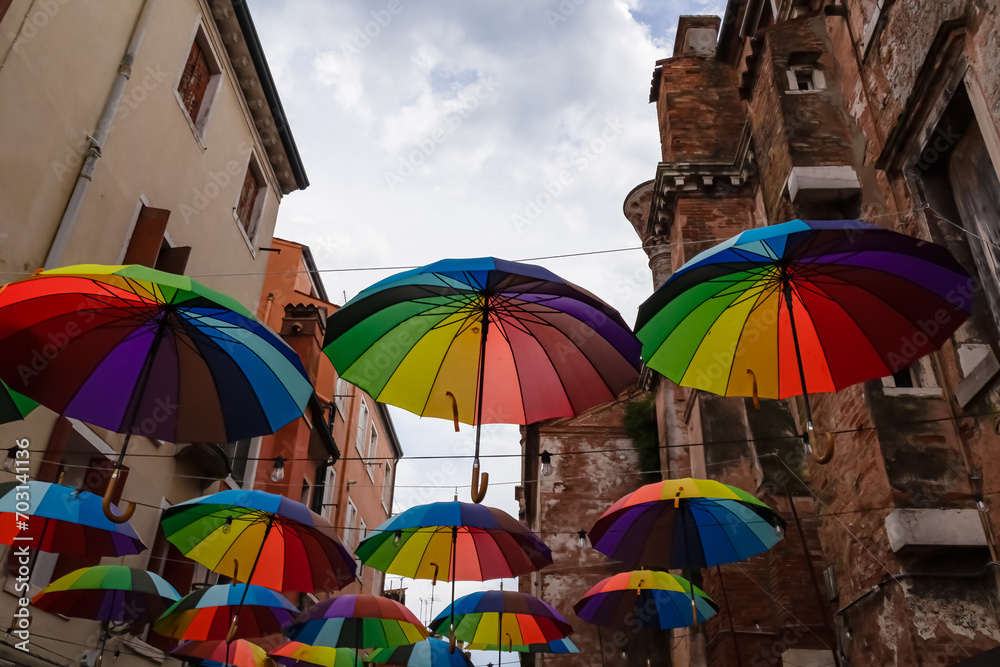 Gorgeous bursts of colors from a vibrant assortment of umbrellas embellishing the clear blue sky in the picturesque town of Chioggia, Venetian Lagoon, Veneto, Italy. Walking in old town. Decoration