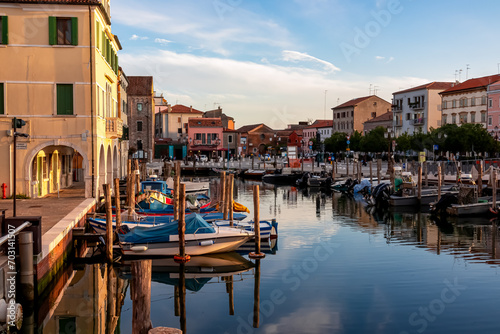 Scenic view of peaceful canal Vena at sunrise in charming town of Chioggia, Venetian Lagoon, Veneto, Italy. Small boats floating in calm water. Enchanting reflections create atmosphere of tranquility © Chris