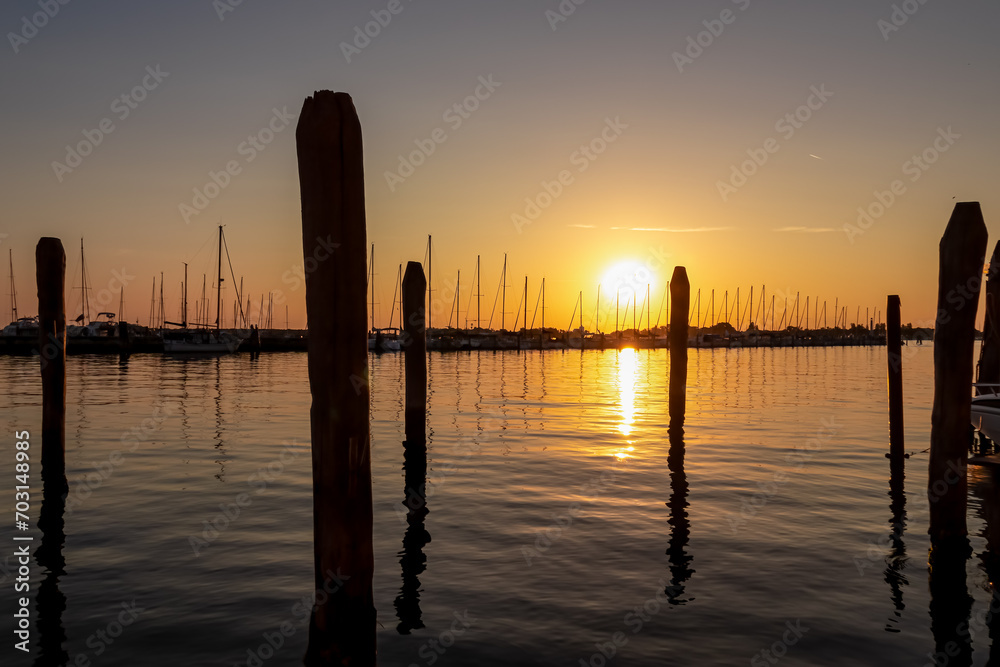 Silhouette of bricolas and boats in picturesque port of charming town of Chioggia at sunrise, Venetian Lagoon, Veneto, Italy. Warm colors and tranquil atmosphere in summer. Magical bay in Adriatic sea