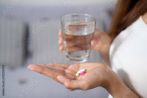Close up of three pills in woman hand and blurred a glass of water at bedroom background.