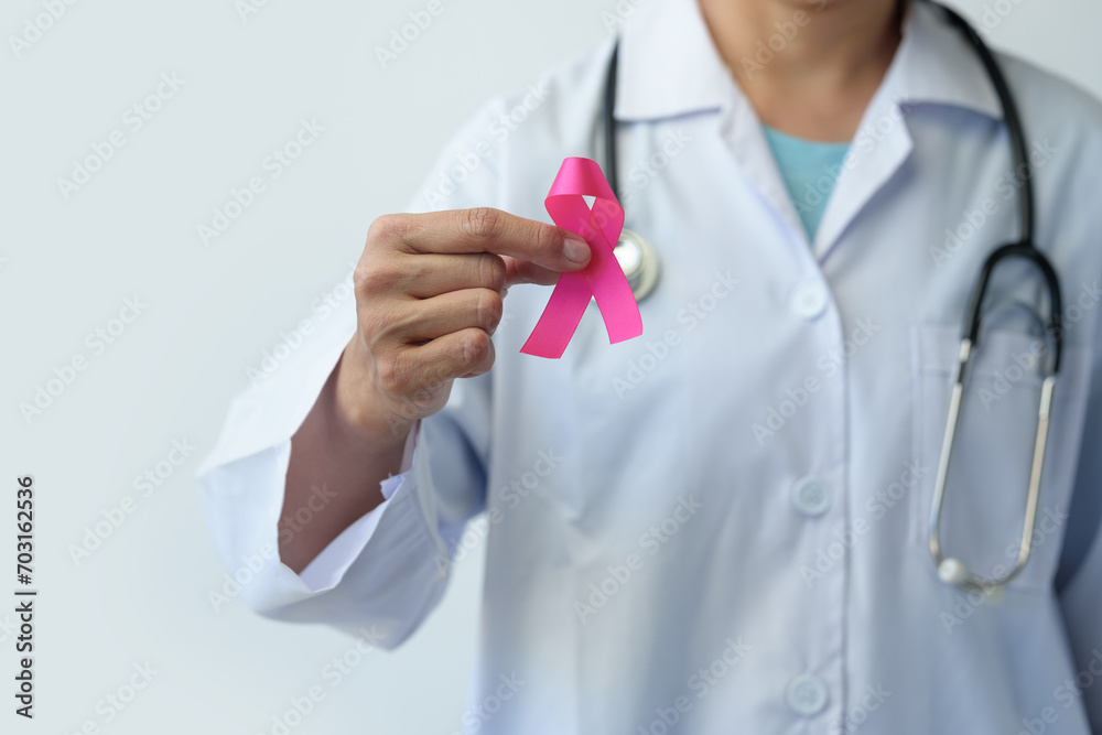 Breast cancer campaign Cropped image of woman's hand in doctor's uniform with pink ribbon in hospital showing fight To save lives and illnesses from cancer World cancer day concept, health insurance. Breast cancer campaign Cropped image of woman's hand in doctor's uniform with pink ribbon in hospital showing fight To save lives and illnesses from cancer World cancer day concept, health insurance.