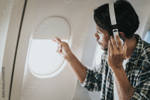 Asian man on an airplane looking out the window with headphones on, possibly enjoying music or an audiobook during his flight. photo