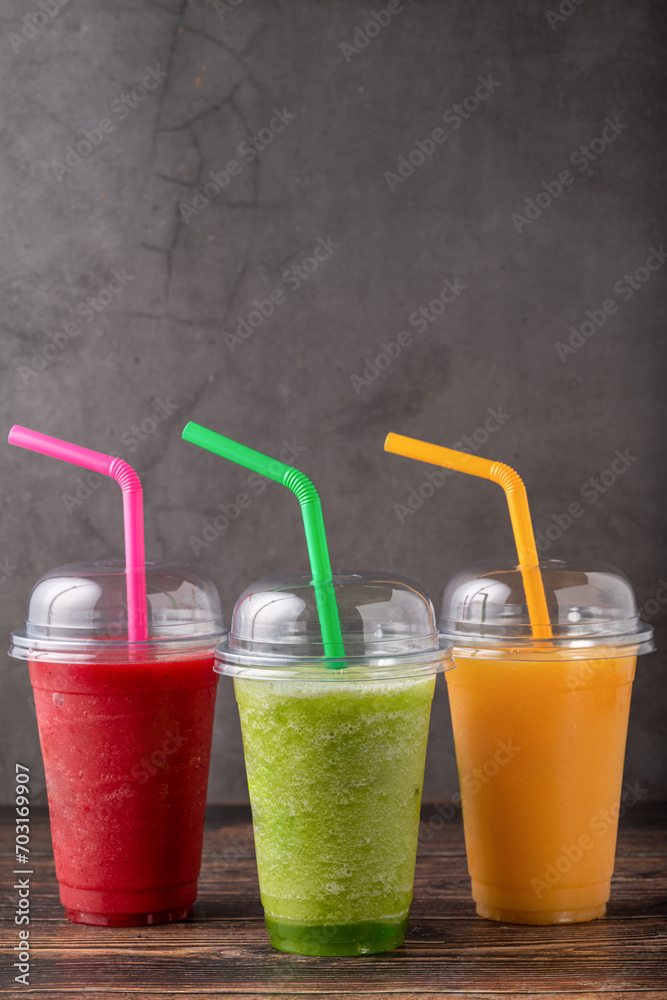 Three different fruit smoothies in plastic take away glasses on wooden background Three different fruit smoothies in plastic take away glasses on wooden background