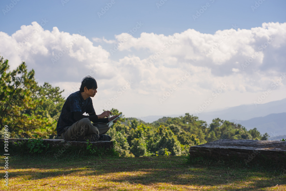 landscape and travel concept with solo freelancer man sit on wooden and use tablet work from outdoor with layer of mountain background
