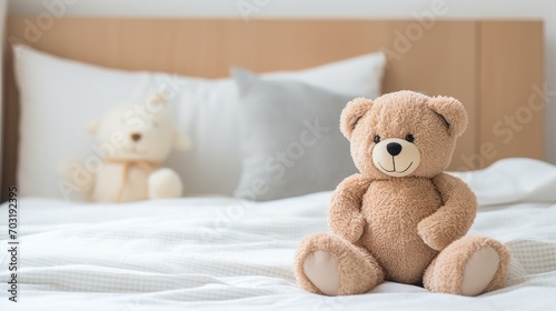 A cute brown teddy bear sits on a white bedspread with a white teddy bear in the background