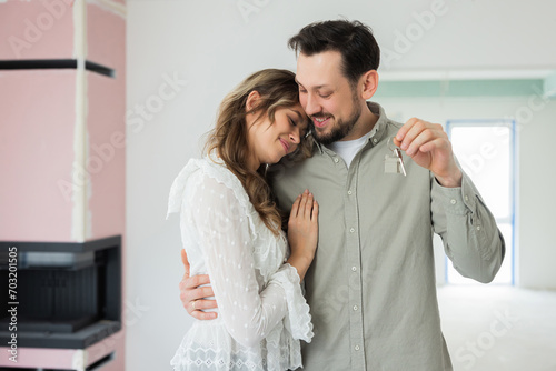 Emotional love concept delighted woman and man husband and wife buying new house apartment demonstrating showing keys at camera from new spacious home smiling hugging new level of life first purchase.