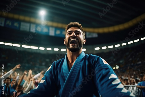 Caucasian male judoist in a blue uniform rejoices after winning a tournament in a stadium filled with spectators