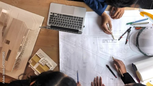 Engineer and Architect Team look at building blueprint from above. Top view of a group of businesspeople talking about blueprints when brainstorming in a meeting using a laptop and calculator. photo