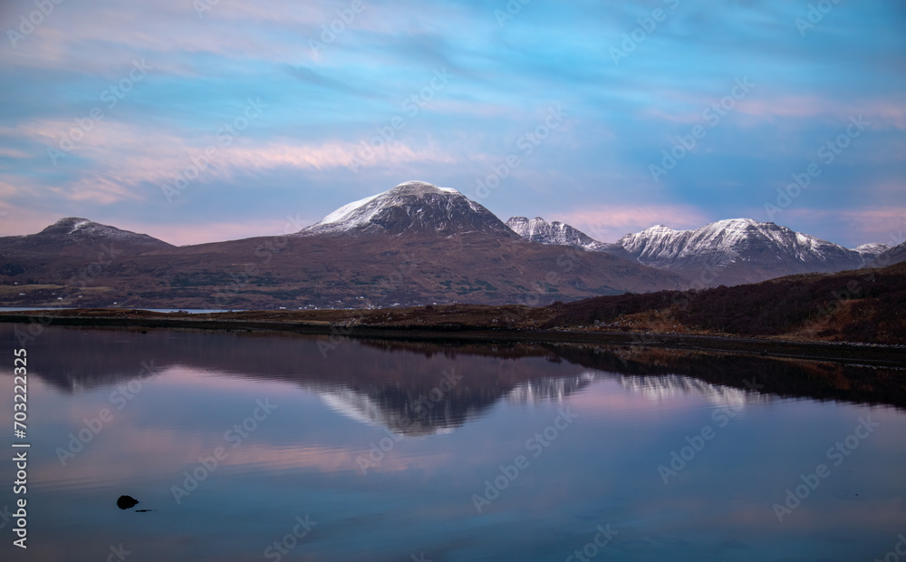 Sun setting over Beinn Alligin, mountains in Torridon, with natural water reflection on the loch