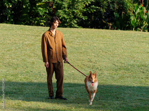 Portrait of handsome Chinese young man with curly hair standing with his rough collie dog on green grass field in sunny day  male fashion  cool Asian young man lifestyle  harmony man and pet.