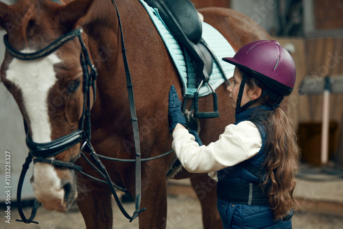 Little girl, kid in helmet taking care after horse, showing her love. Child training horseback riding in special arena, pavilion. Concept of sport, childhood, school, course, active lifestyle, hobby © master1305