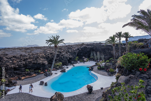 Pool of blue waters and palemeeras, outside the cave of Los Jameos del Agua. Light at the end of the cave. Sky with big white clouds. Lanzarote, Canary Islands, Spain.