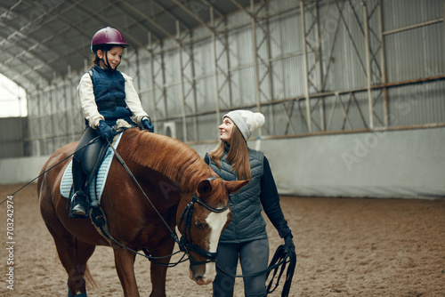 Young woman, teacher, instructor teaching little girl horseback riding. Child sitting in paddle, practicing. Education. Concept of sport, childhood, school, course, active lifestyle and hobby