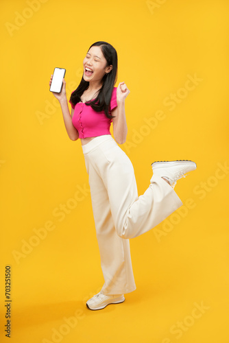 full-body portrait of an happy Asian woman holding a cell phone on a yellow background