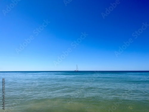 small white sailboat silhouette at the blue sea horizon, blue seascape, clear blue sky