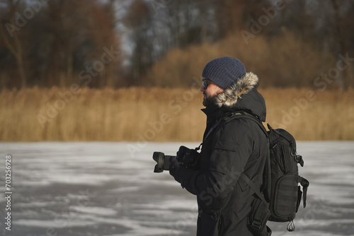 Male landscape photographer outdoors with a camera in his hands, side view. © Dmitri