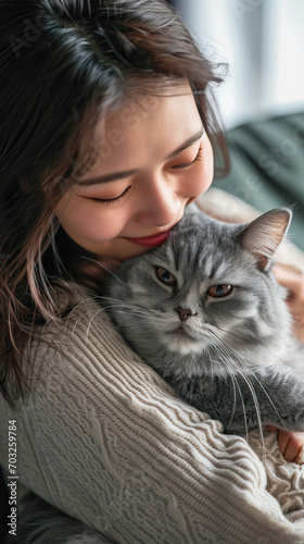 Happy Young Asian Woman Embracing a Cute Grey Persian Cat on the Couch in the Living Room. Adorable Domestic Pet Companionship.