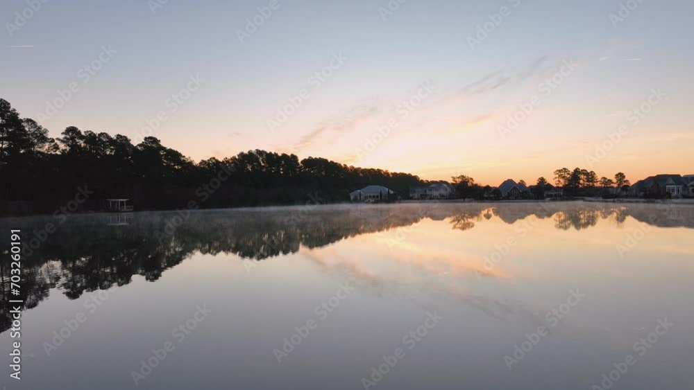 Serene lake at sunrise with mist rising from warm waters against a cool air backdrop, reflecting the awakening sky and silhouetted trees. Serene lake at sunrise with mist rising from warm waters against a cool air backdrop, reflecting the awakening sky and silhouetted trees.