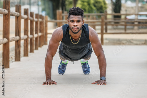 Determined black sportsman doing plank on ground in city park