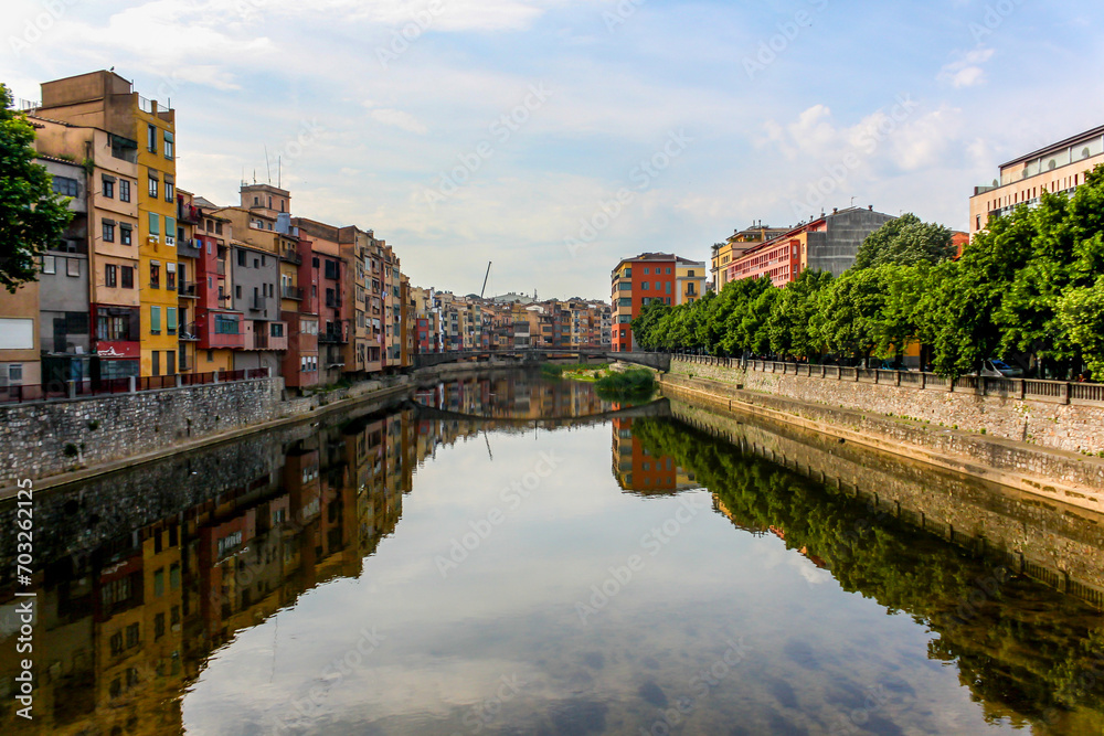 View of the Onyar River in Girona, Spain with the reflection of the buildings and bridge.
