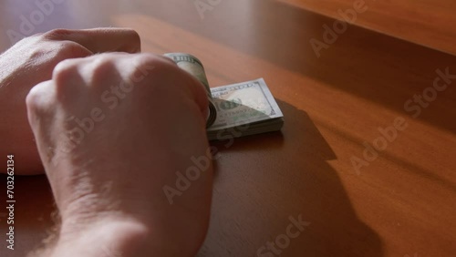 A man's hand puts one hundred dollar bills on a wooden brown table. A woman's hand rests a car key on top of them. The keychain is taken away and the money too. The concept of buying a car. photo