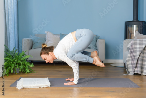Young woman practicing yoga bakasana or crow pose at home. Concept of a healthy lifestyle, women's wellness, and active recreation. © Iaroslava Zolotko