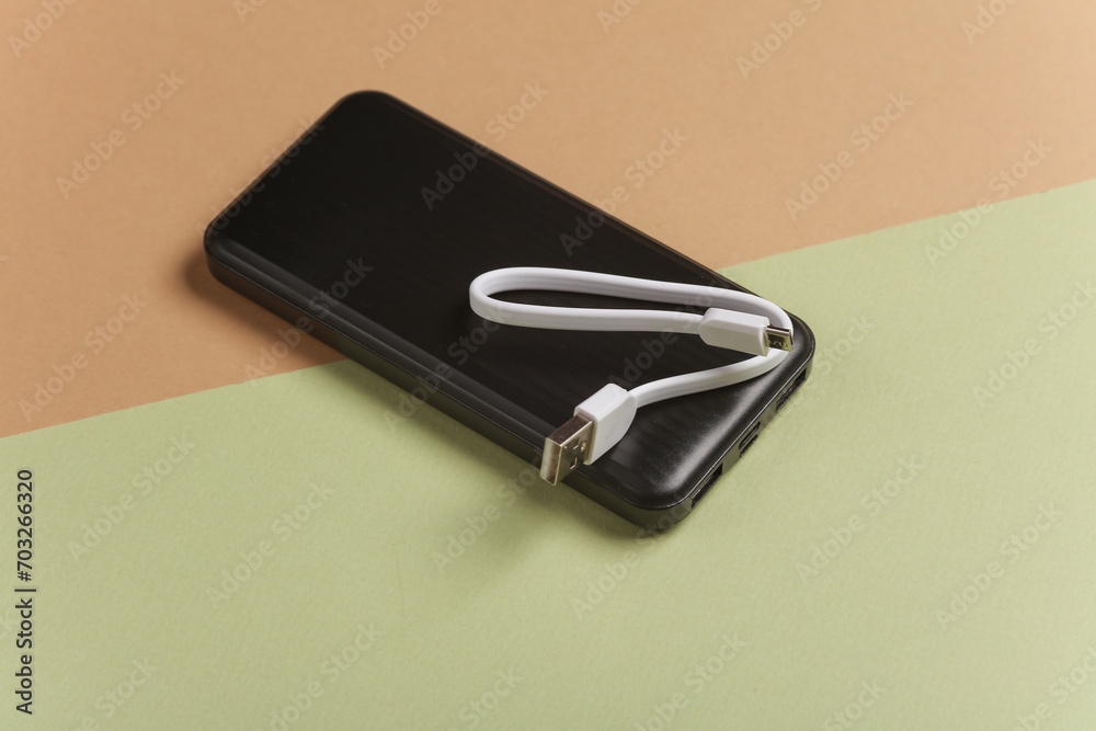 Black power bank with cable on green beige background Black power bank with cable on green beige background