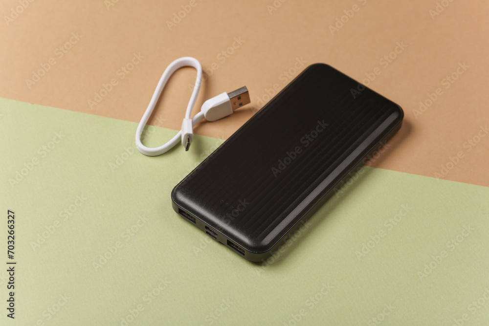 Black power bank with cable on green beige background Black power bank with cable on green beige background