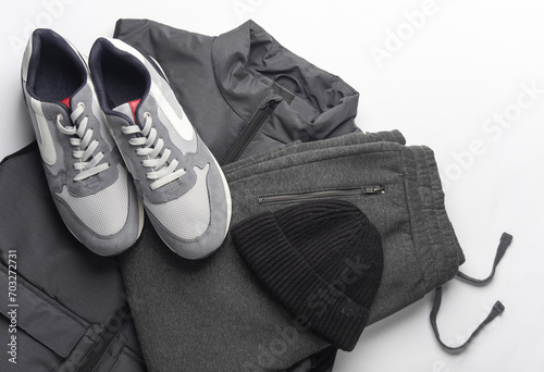 Men's sleeveless down jacket, sweatpants, sneakers and hat on a white background. Top view. Sportswear