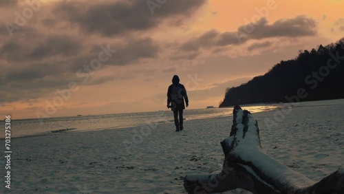 Young male in coat standing  and looking at the horizon with during the bright sunset. Concept of solitude to non tourist spots places.