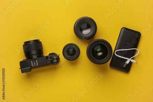 Professional modern mirrorless camera with set of lenses and power bank on yellow background. Top view