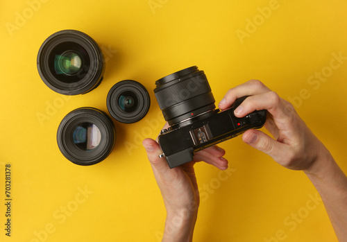Hands holding a modern mirrorless camera with lenses on yellow background