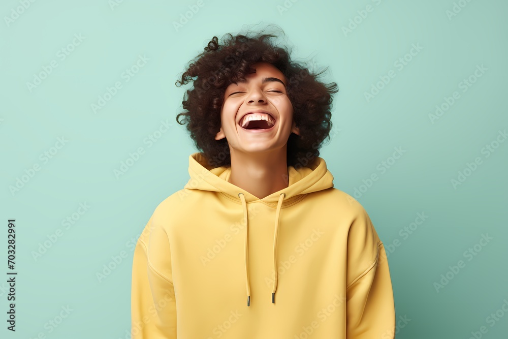 A teenager beaming happily in a soft teal hoodie against a light yellow background. A teenager beaming happily in a soft teal hoodie against a light yellow background.