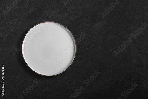Handmade empty ceramic plate top view with copy space on dark concrete table. Minimalism. Eco friendly ceramics handcraft tableware.