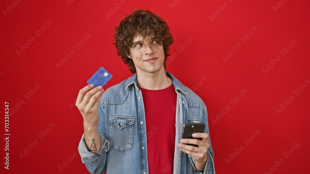 Smiling man with curly hair holding credit card and smartphone on red background Smiling man with curly hair holding credit card and smartphone on red background