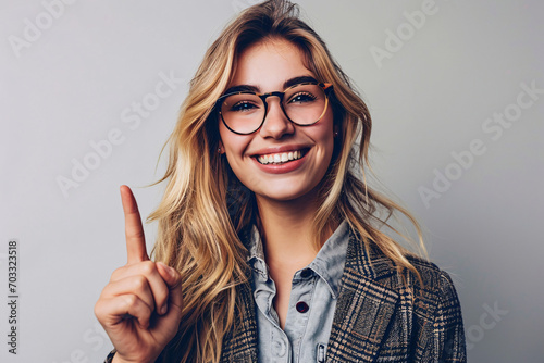 Cheerful young woman with glasses pointing upwards with one finger photo