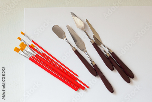 A set of painting brushes and palette knives on a white canvas